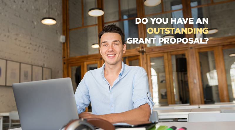 Man at his desk, smiling at the camera because he's written a winning grant.